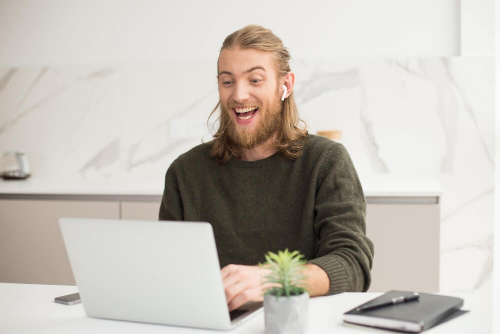 A young cheerful man sitting table with a laptop | TechReviewGarden
